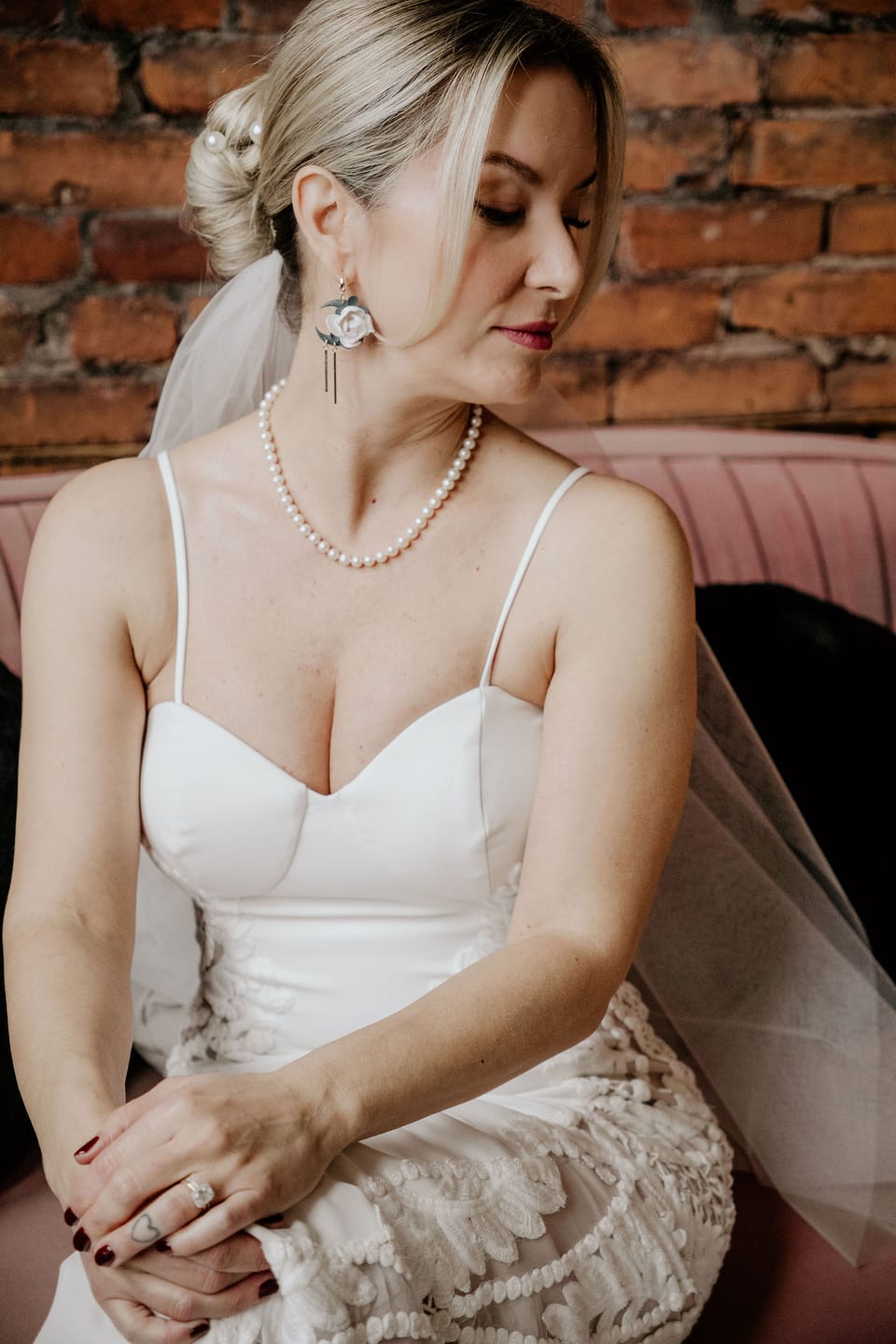 Bride seated in her lace gown against an exposed brick wall.